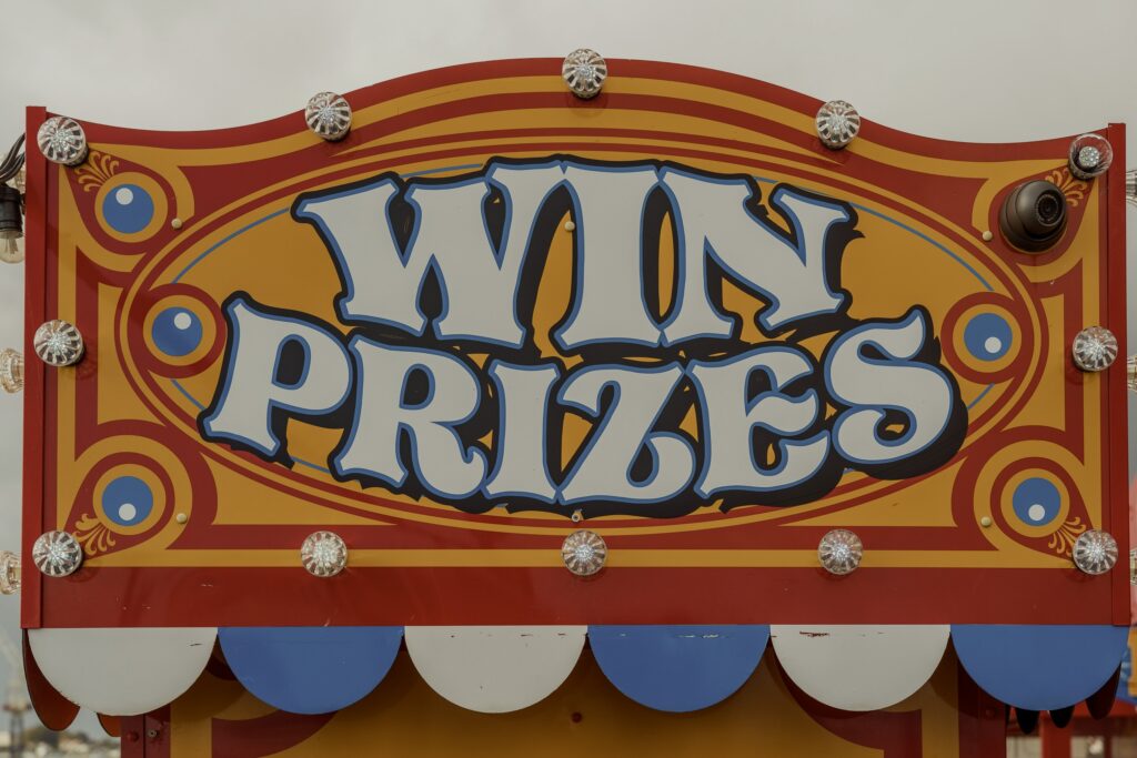 Retro carnival sign lit with bulbs reading “WIN PRIZES,” evoking the spectacle of awards culture