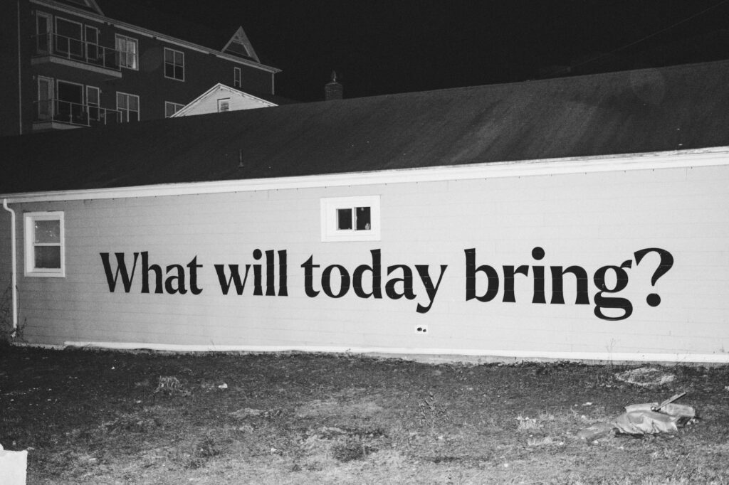 Black and white photo of a building with "What will today bring?" painted on the wall, reflecting producer prep and planning for audio post.