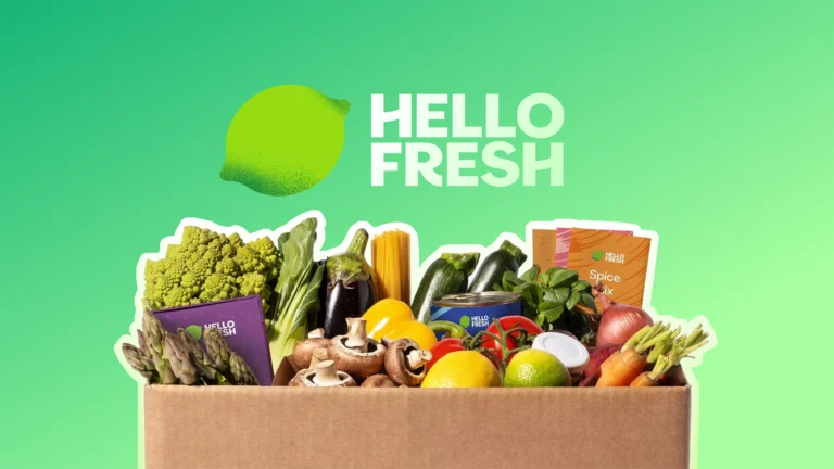 Hello Fresh logo above a box filled with fresh vegetables, fruits, and meal kit ingredients on a green background.