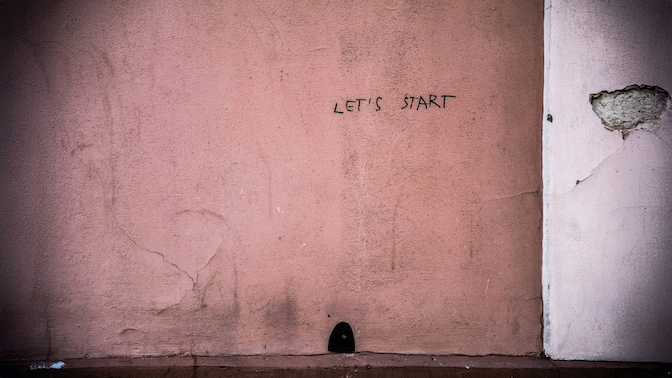 Minimalist photo of a cracked pink wall with graffiti reading 'LET'S START', used in an article about NEOM and The Line exploring silence as a premium commodity in the city’s sound design.
