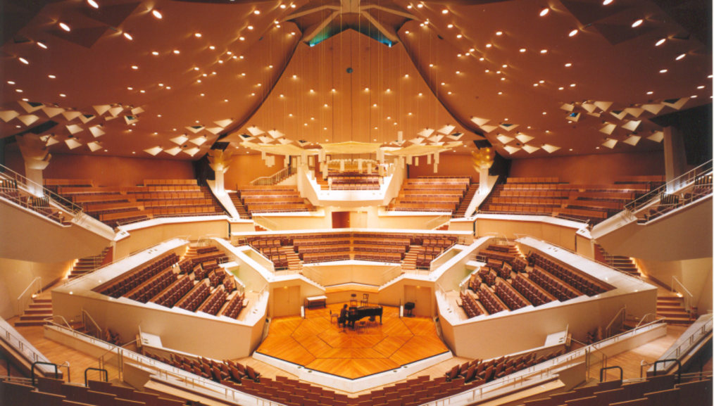 The empty interior of the iconic Berlin Philharmonie. The asymmetric, tiered seating and complex ceiling panels are visible, highlighting the hall's revolutionary design as an optimised environment where sound is diffused evenly to every listener